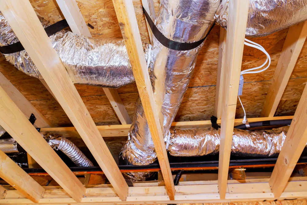 HVAC ductwork with foil insulation in a wooden attic structure.
